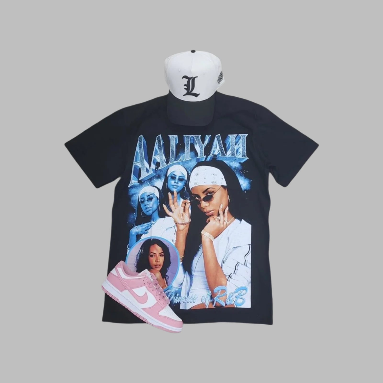 Black t-shirt with graphic design, white cap, and pink sneaker on a gray background